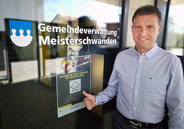«Wir wollen Vorbild sein»: Meisterschwandens Gemeindepräsident Ueli Haller vor einem Coronaplakat beim Gemeindehaus. Foto: Fritz Thut
