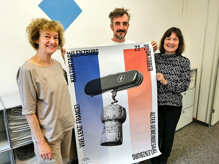 Champagnerzapfen und Schweizer Militärsackmesser: Sylvia Voegeli, Stéphane Vincent und Beatrice Burgherr vom Organisationskomitee der Kulturtage Lenzburg «Vive Lenz’France» mit dem Veranstaltungsplakat. Foto: Fritz Thut
