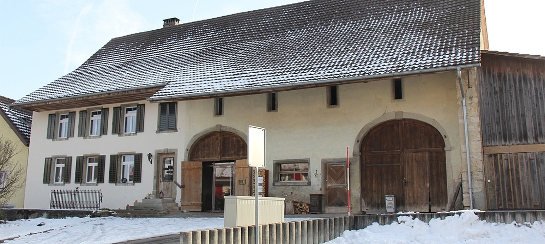 Das Gebäude wurde 1836/37 als bäuerlicher Vielzweckbau errichtet: Es ist klar gegliedert in Wohnteil, Futtertenn, Stall, Tenn und Schopf. Es stellt ein typisches Juragiebelhaus dar. Als südliche Begrenzung des Dorfplatzes nimmt es in leicht erhöhter Lage eine äusserst wichtige Stellung im Ortsbild ein. 2014/15 wurde das Gebäude renoviert.
