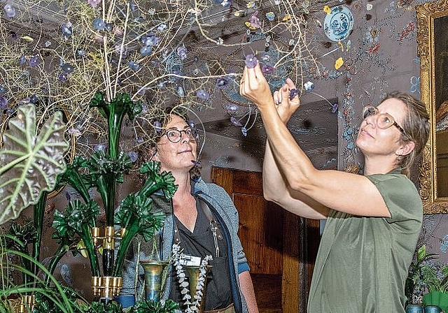 Filigrane Kunst an der Decke: Schlossfloristin Manuela Fischer (links) ist begeistert ob der Ideenvielfalt von Meisterfloristin Evelyn Krebs mit der floralen Interpretation der damaligen Geschehnisse in der Salis-Stube. Foto: Peter Winkelmann
