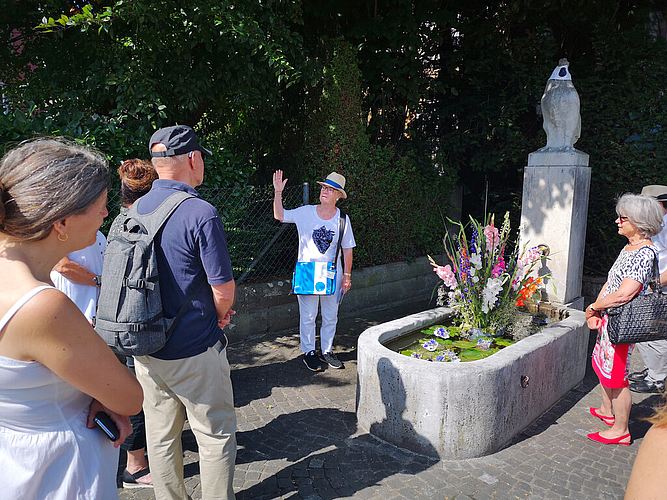 Güggel mit Gesichtsschutz: Brunnenführung mit Bodil Wälli beim Güggelbrunnen. Foto: Fritz Thut
