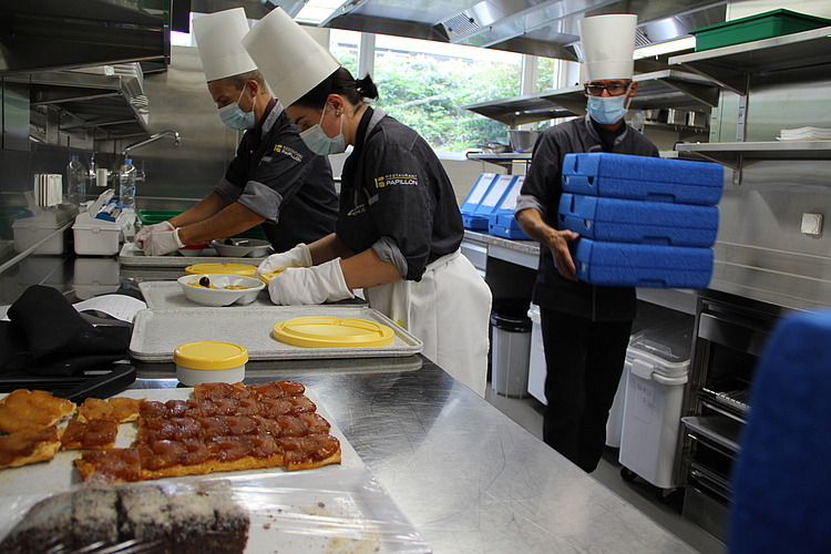 Die Mahlzeiten werden frisch zubereitet: Die Küchen-Crew beim Verpacken des aktuellen Menüs – Pouletgeschnetzeltes an Currysauce mit Früchtegarnitur, Suppe, Salat und Dessert. Foto: Carolin Frei