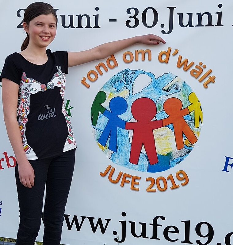 <em>Zurecht stolz auf das eigene Werk:</em> Klara Wehrle posiert vor dem von ihr entworfenen Jugendfest-Logo. Foto: zvg
