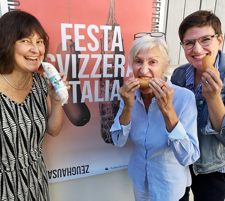 <em>Zum Reinbeissen: </em>Beatrice Burgherr, Andrea Bühler und Cynthia Luginbühl, Mitglieder der organisierenden Kulturkommission, knabbern vor dem Plakat der «Festa Svizzera Italia» symbolisch in Salami und Servelat. Foto: Fritz Thut