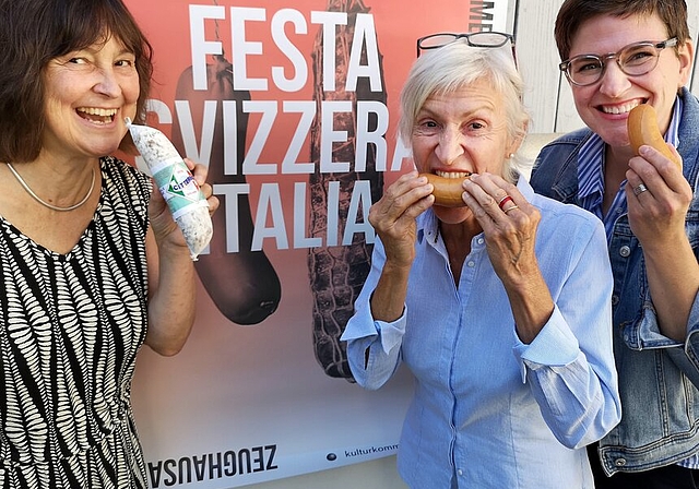 <em>Zum Reinbeissen: </em>Beatrice Burgherr, Andrea Bühler und Cynthia Luginbühl, Mitglieder der organisierenden Kulturkommission, knabbern vor dem Plakat der «Festa Svizzera Italia» symbolisch in Salami und Servelat. Foto: Fritz Thut