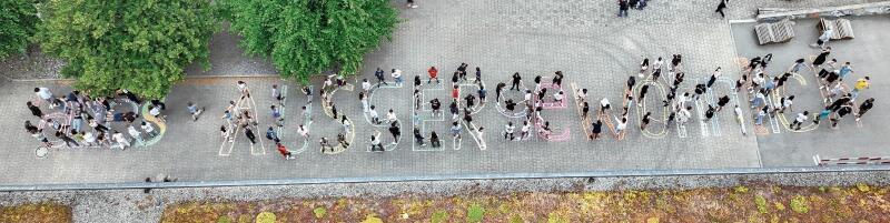 Zwischen Mehrzweckhalle und Haus 4: Schüler bilden den Schriftzug «AllesAusserGewöhnlich», das Motto des Seenger Jugendfestes 2024.Drohnenfoto: Schule Seengen