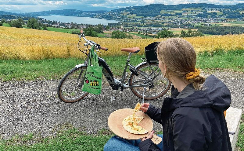 Regionale Köstlichkeiten an den Etappenzielen: FoodTrial-Seetal-E-Bikerin geniesst die Aussicht über den Hallwilersee und das gereichte Häppchen. Foto: zvg
